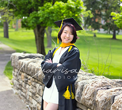 Graduate student in robe and cap leaning against a wall